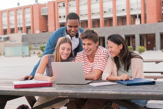 A group of students using a laptop while searching for information for a project outdoors.