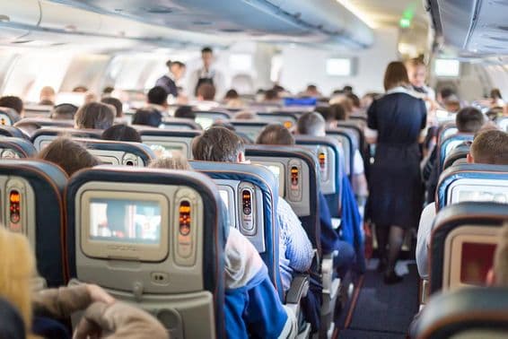 Interior of an airplane with people, seats, and flight attendants.