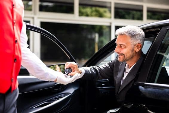Businessman hands over car keys to valet at hotel parking.