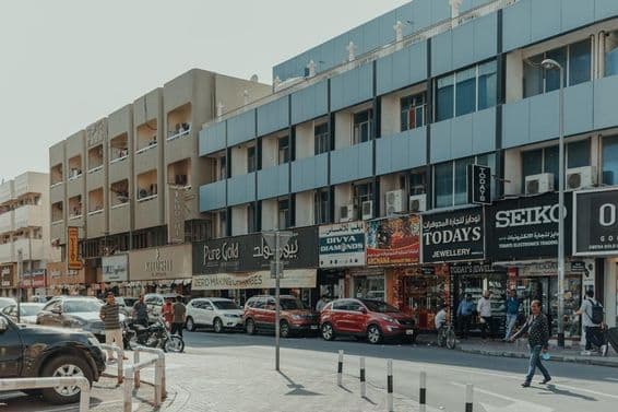 Busy street in Bur Dubai with jewelry stores, pedestrians, and cars on a sunny day.