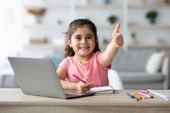 A young Arabic girl gives a thumbs up while learning at home with a laptop.