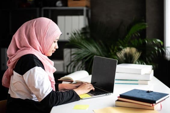 A beautiful Muslim woman studies at home using a laptop.