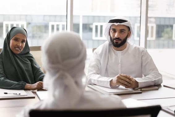 Male and female Arab colleagues at an office desk conversing with a seated partner.