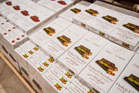 Dubai chocolate bars filled with kunafa and pistachio stacked on a store shelf.