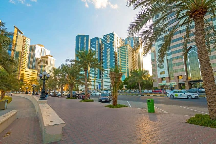 Sharjah city skyline at sunrise with golden light reflecting off modern skyscrapers.