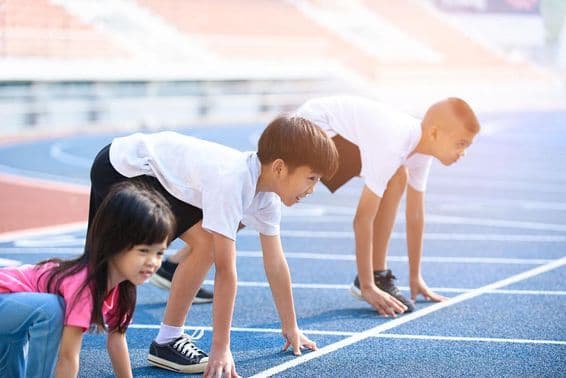 Children preparing for a race on a blue track.