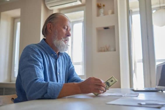 Elderly man with a beard and wrinkled hands counting Russian rubles.