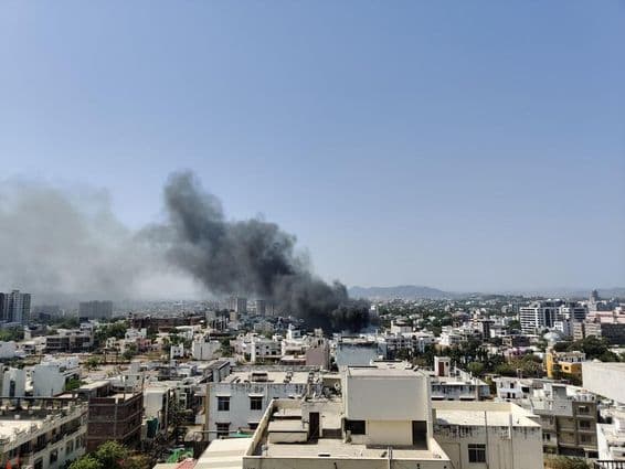 A thick black smoke column rises above the city.