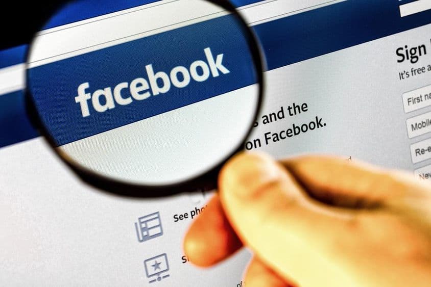 Facebook homepage screenshot on a monitor through a magnifying glass.
