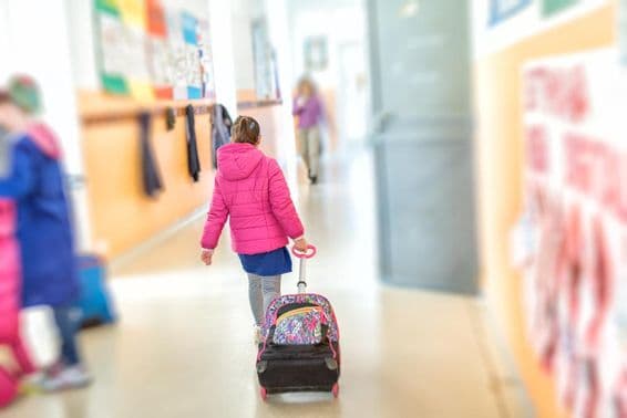 A young girl pulls a rolling school backpack.