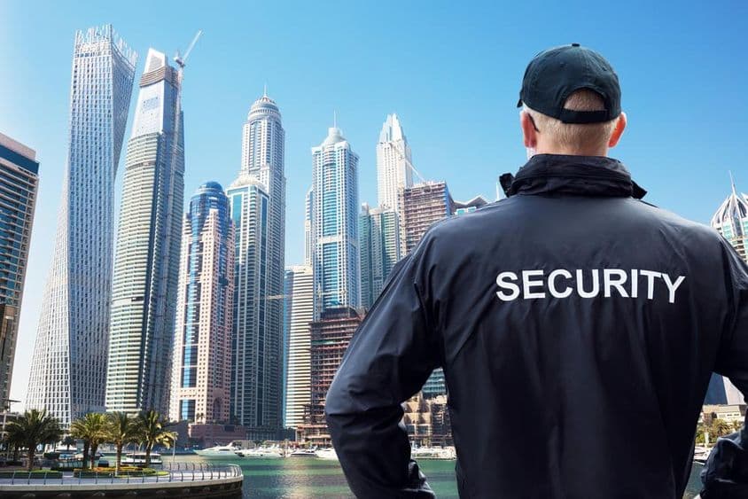 Male security guard standing and watching the cityscape from behind.