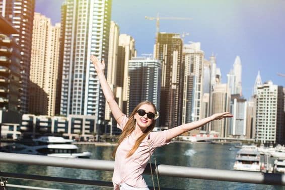 Sunshine illuminates a stylish woman raising her hand on a bridge somewhere in Dubai.