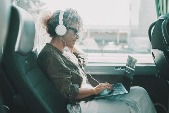 Young woman working on a laptop with headphones on a bus seat.