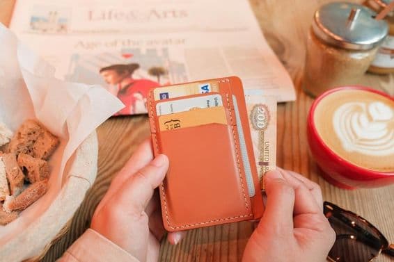 A hand pulling out 200 United Arab Emirates dirhams from a brown leather cardholder.