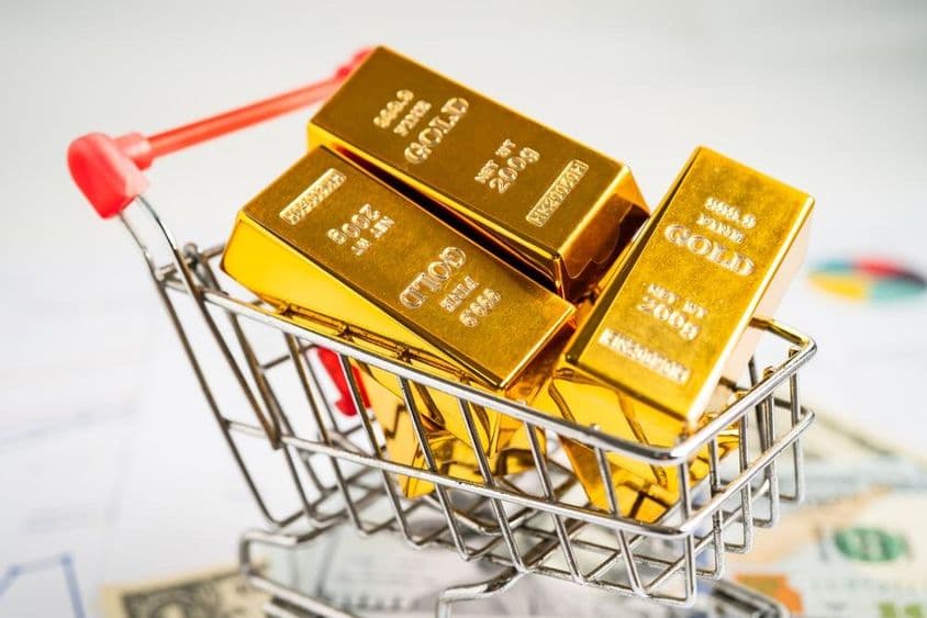 Gold bar in a shopping cart on US dollar bills.