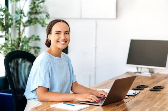 Confident woman sitting at a modern office desk, looking into the camera, and smiling friendly.