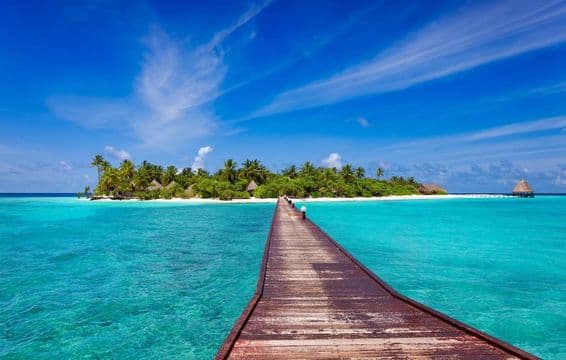 Pier over blue ocean leading to tropical island's sandy beach, Maldives.