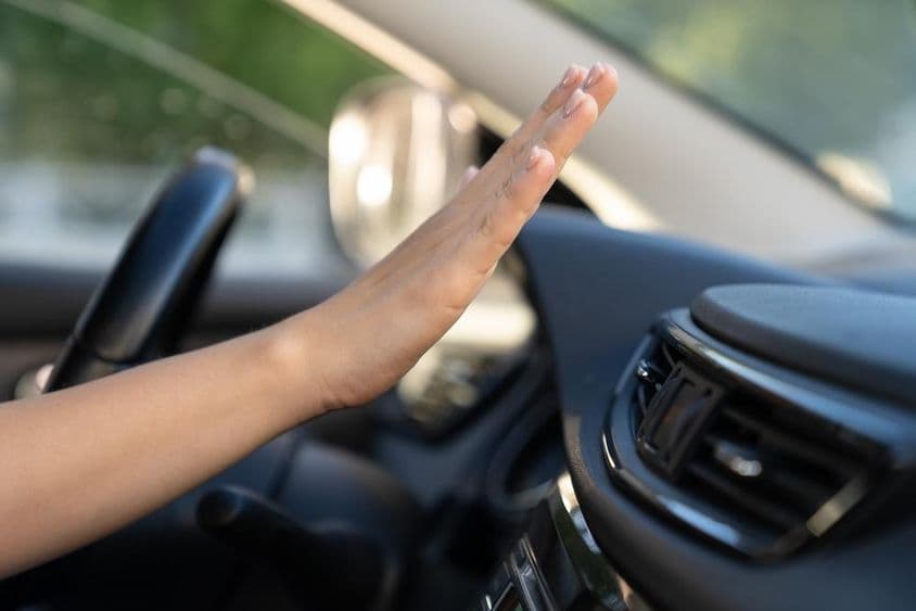 A woman's hand checks the air conditioning panel in a car.