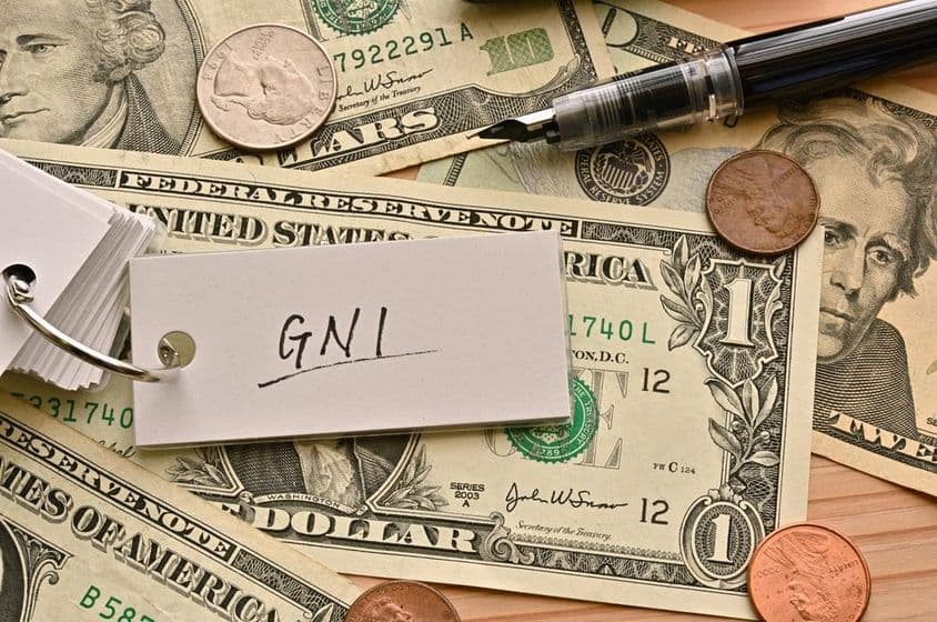 The financial term GNI written atop dollar bills on a table.