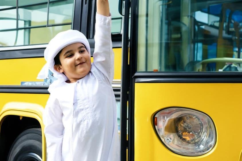 Arab elementary school student near a yellow school bus.