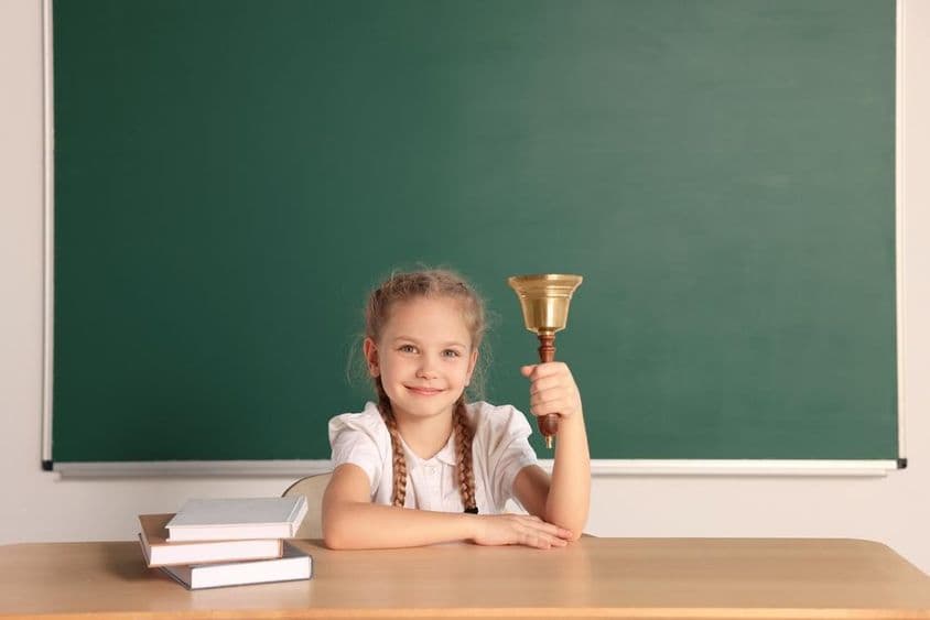 Student sitting at desk with school bell in a classroom.