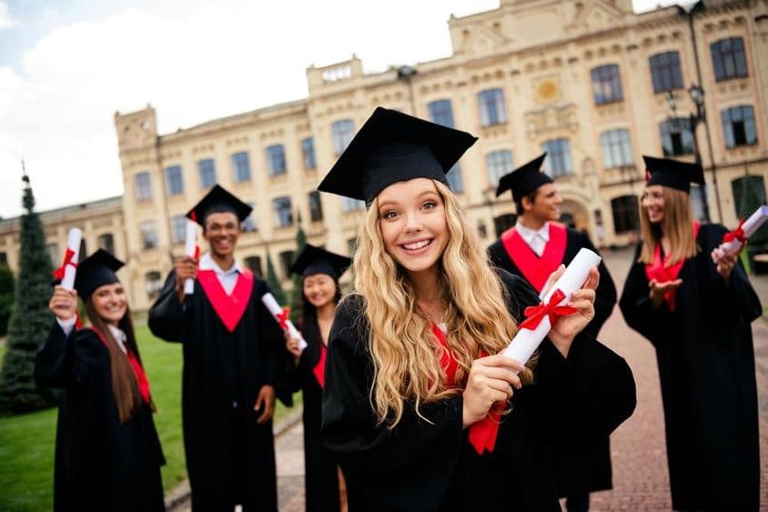 Cheerful young graduates celebrating academic achievements outdoors.