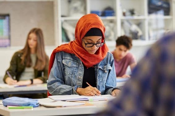 Young female student studying in a hijab while taking notes.