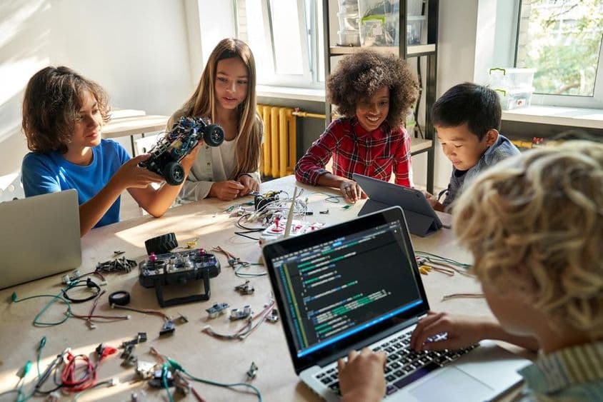 School children building robotic cars using computers and programming.