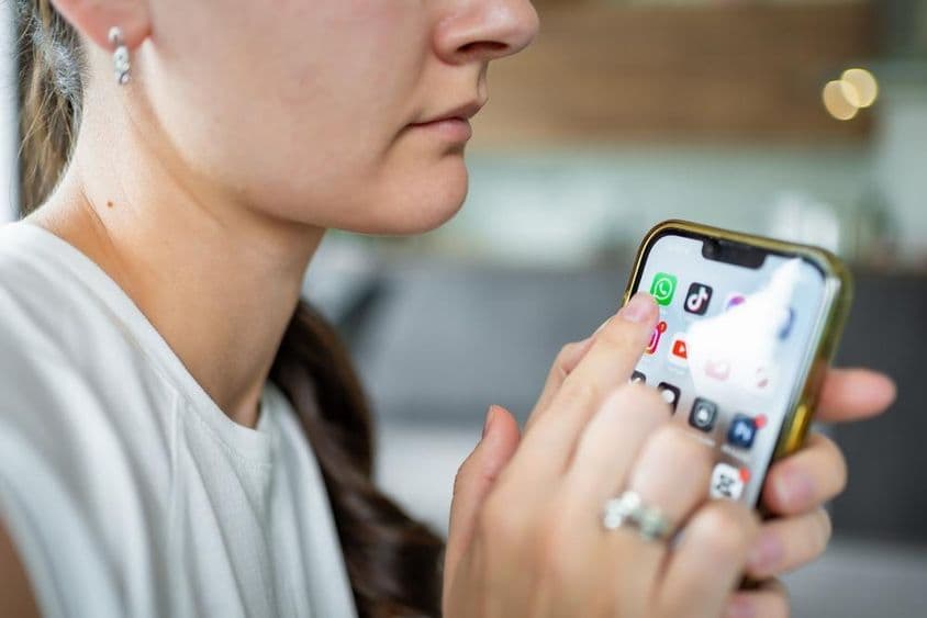 Woman holding an iPhone with WhatsApp chat application on screen.