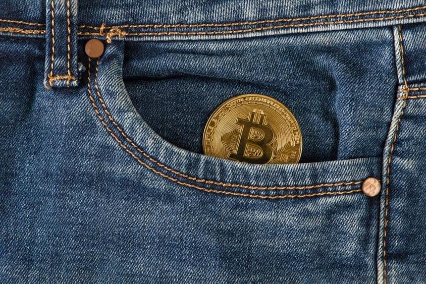 A gold bitcoin coin lies in a jeans pocket.
