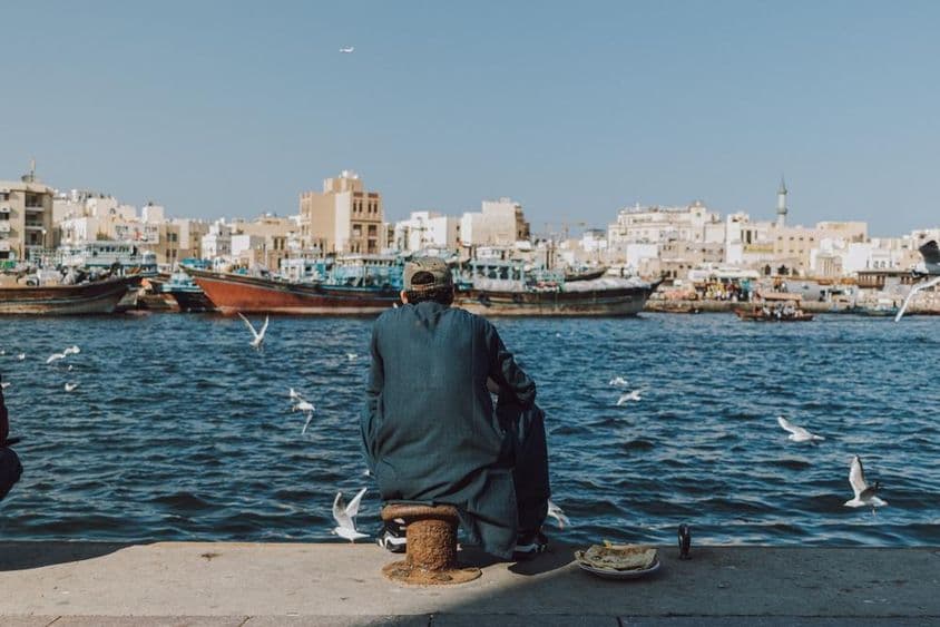 Man enjoying the waterfront view with boats and seagulls at Dubai Creek.