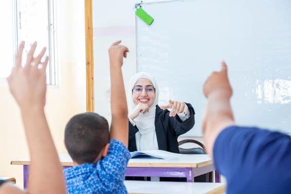 Students raising hands, indicating present and responding to the teacher.