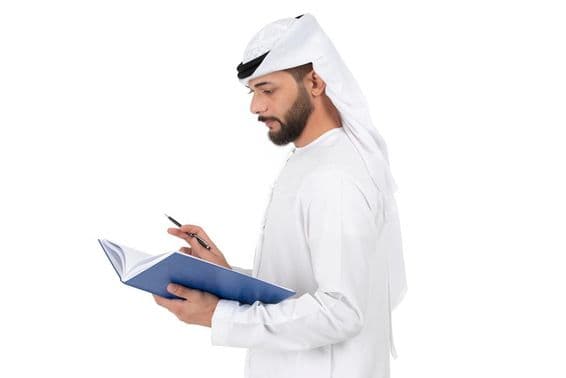Young Arab teacher standing and writing in the book.