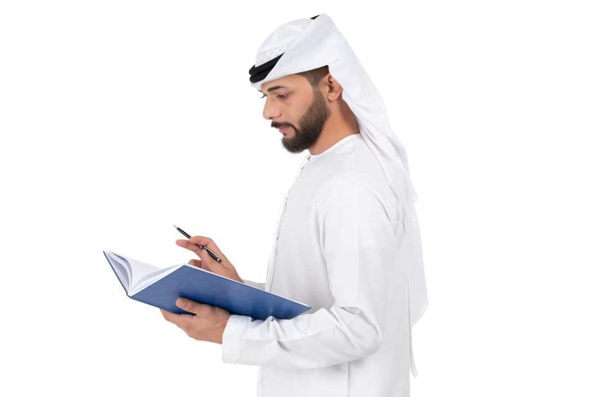 Young Arab teacher standing and writing in the book.