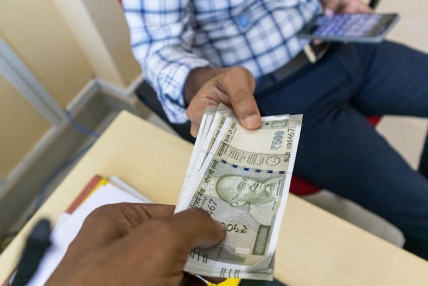 A person handing over a 500-rupee Indian banknote to another person.