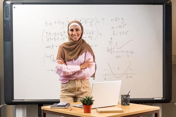 Arab female teacher in hijab standing in classroom.