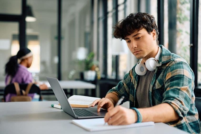 University student using a laptop while writing.