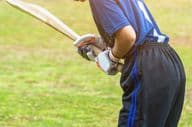 Asian young female cricketer in protective gear hitting a ball with a bat on the field.