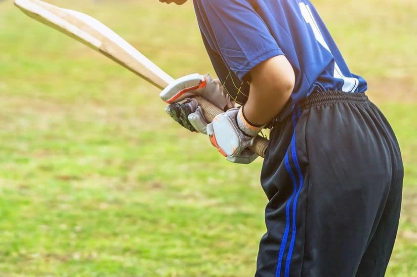 Asian young female cricketer in protective gear hitting a ball with a bat on the field.