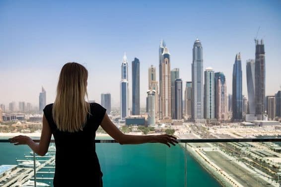 A woman in black with a pensive look on a balcony overlooking the skyscrapers of Dubai, United Arab Emirates.