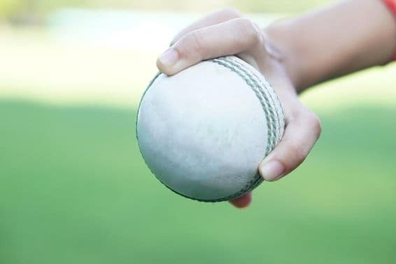 A cricketer holding a white leather cricket ball.