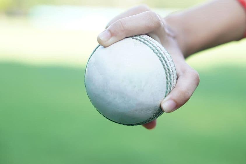 A cricketer holding a white leather cricket ball.