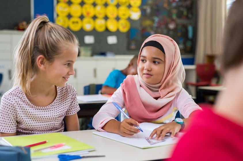 Asian Muslim schoolgirl sitting near classmate during class.