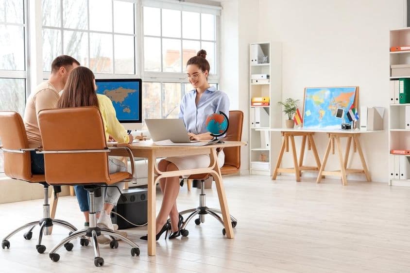 Travel agent working on a laptop with a young couple at the desk in an office.