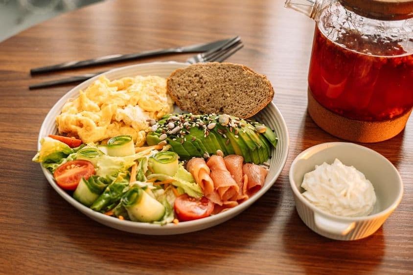 Healthy breakfast with eggs, avocado, greens, salad, and raspberry tea.