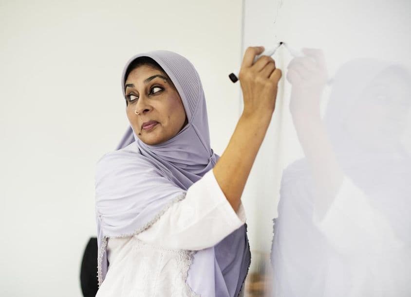 Muslim teacher writing on a whiteboard.