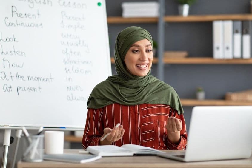 Smiling female Arab teacher in headscarf initiating video call.