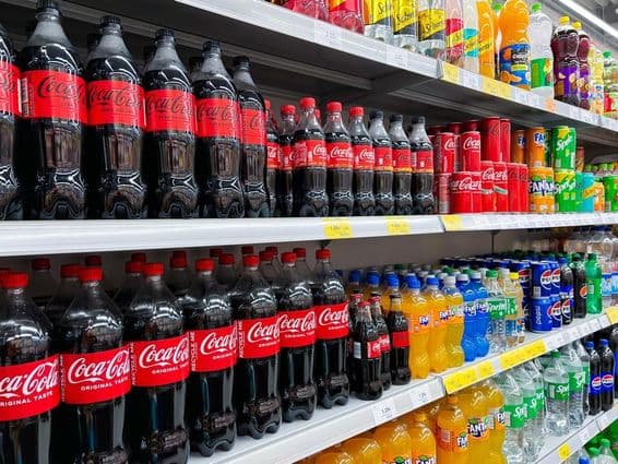 Row of cola bottles on a supermarket shelf.