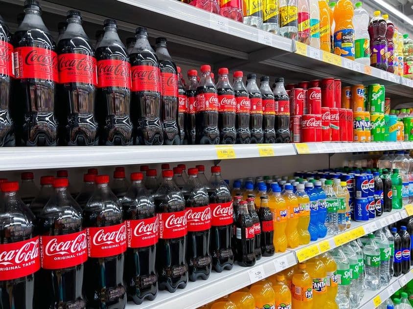 Row of cola bottles on a supermarket shelf.
