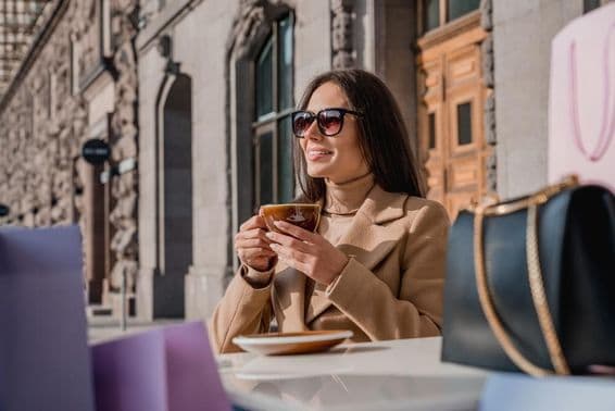 A girl wearing sunglasses drinking coffee.